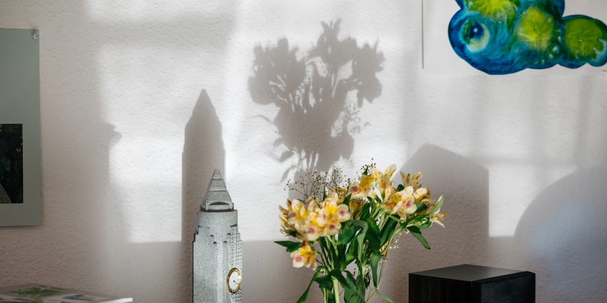 Blumenstrauß und ein Modell des Frankfurter Messeturms auf dem Fensterbrett, die Schatten fallen auf die Wand