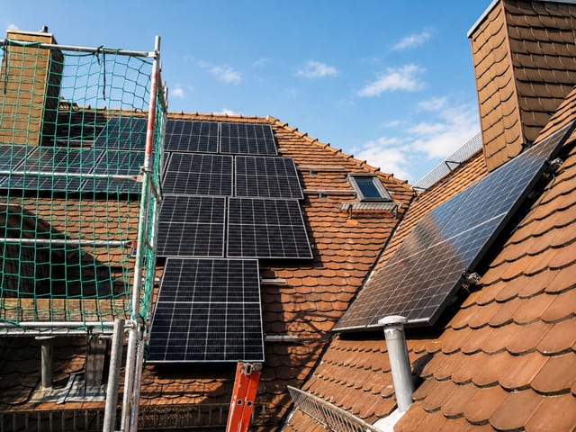 Solarmodule auf einem Ziegeldach, davor ein Gerüst mit Netz