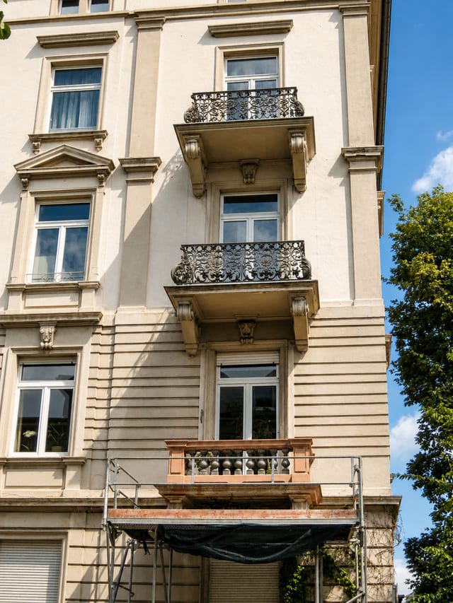 Helle Gründerzeitfassade mit schmiedeeisernen Balkongittern, links ein Baum
